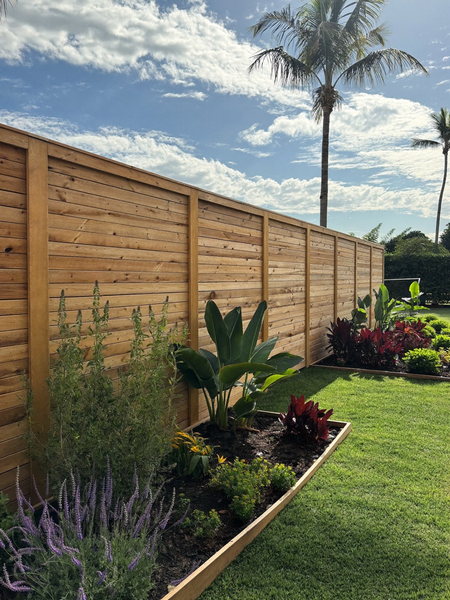 A freshly built horizontal-slat cedar privacy fence beside raised garden beds and new sod.